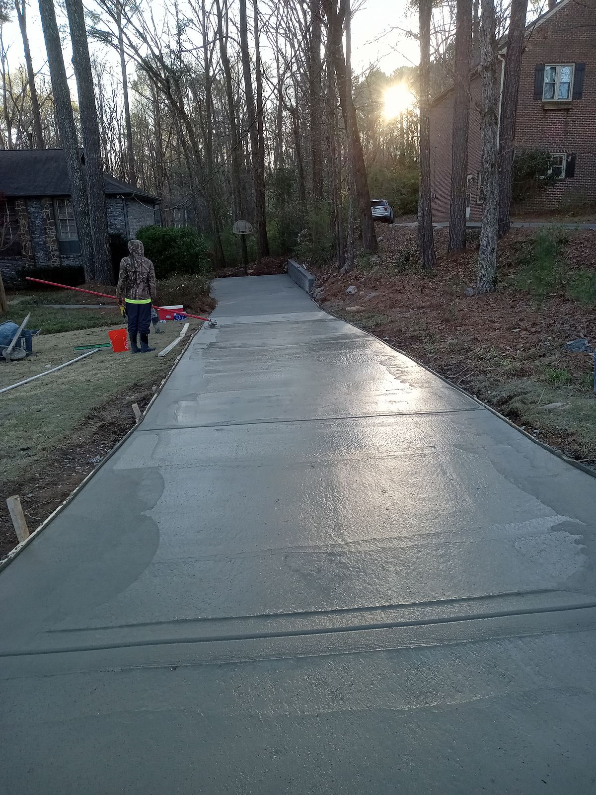 Concrete crew member finishing a freshly poured residential driveway at sunset